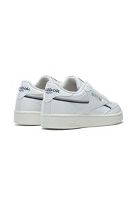 Baskets blanches avec un dessus en cuir lisse, une ligne d'accent bleu marine et une semelle en caoutchouc texturé. Présente le logo Reebok et une étiquette végan sur le talon.