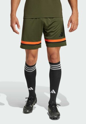 Olive green athletic shorts with orange and black stripes, paired with black knee-high socks featuring white stripes and branding.