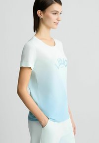 T-shirt bleu clair, dégradé, à manches courtes, avec un col rond, arborant un logo "LIU JO" subtil dans une teinte plus foncée. Tissu en coton doux.