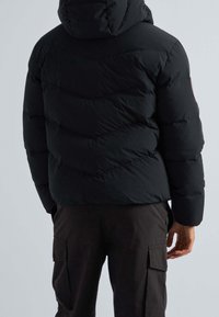 Veste matelassée noire avec capuche, présentant un motif matelassé, des poignets élastiques et une texture lisse. Vue de dos montrant le logo sur la manche gauche.