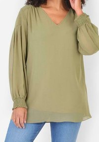 Olivově zelená halenka s V výstřihem, plisovanými dlouhými rukávy a pružnými manžetami. Látka má lehkou, hladkou texturu. Volný střih.
