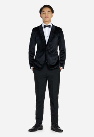 Chaqueta de esmoquin de terciopelo negro con solapas de satén, camisa blanca de vestir, pajarita negra, pantalones de vestir negros y zapatos de cuero negro.