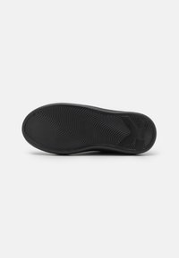 Semelle de chaussure en caoutchouc noir avec des motifs texturés en forme de vagues et un logo de marque. Présente une forme plate et large sans détails accentués remarquables.