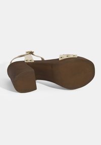 Braun lackierter Schuh mit Absatz und hellbraunen Knöchelriemen. Mit eckiger Spitze und goldfarbenen Hardware-Akzenten an den Riemen. Strukturierte Sohle.