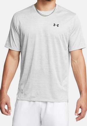 Homme portant un t-shirt de sport à manches courtes gris clair avec un petit logo Under Armour noir sur le côté gauche de la poitrine et un short blanc.