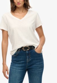 Camiseta blanca de cuello en V hecha de una tela suave, combinada con jeans de mezclilla de tiro alto en azul oscuro y un cinturón negro con detalles en hebilla dorada.