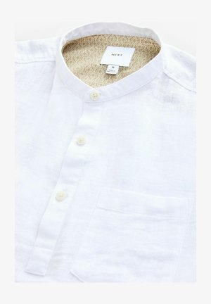 Fehér lenvászon ing mandarin gallérral, elől zsebből és világos gombokból áll. A belsejében bézs mintás bélés található.