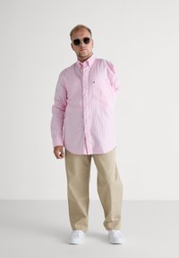 Pink striped long-sleeve shirt with a button-down collar, paired with beige pants and white sneakers. Accessories include black sunglasses.