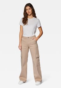 Beige Cargo-Hosen mit weitem Schnitt, mehreren Fronttaschen, kombiniert mit einem schlichten weißen T-Shirt und weißen Sneakers. Glatte Stofftextur.
