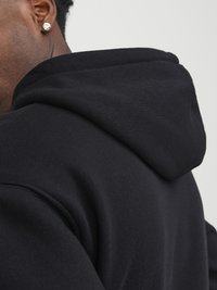 Black hoodie featuring a soft texture, a spacious hood, and relaxed fit. The close-up shows stitching detail on the shoulder and hood.
