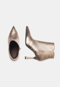Bottines en bronze métallique avec des pointes effilées, texture lisse et épurée, talons aiguilles fins et zips sur les côtés.