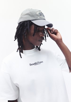 Gray baseball cap with embroidered text, paired with a white t-shirt featuring "Beautiful Future" stitched in black. Close-up view.