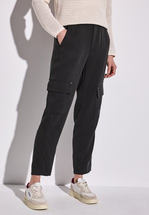 Zwarte cargobroek met zijzakken, elastische tailleband en een ontspannen pasvorm, gecombineerd met witte sneakers met beige en bordeaux accenten.