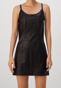 Schwarzes Kunstlederkleid mit dünnen Trägern, geradem Schnitt und zwei kleinen Fronttaschen; glatte Textur und minimale Designdetails.