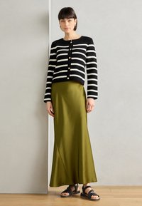 Black and white striped cardigan with gold buttons, paired with a long olive green satin skirt and black strappy sandals.