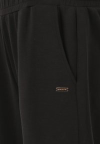 Zwarte joggingbroek van zacht stof met een trekkoord in de taille, twee zijzakken en een klein gouden logo-label nabij de zak.