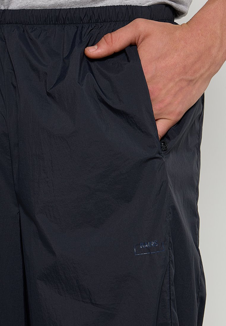 Marineblauwe lichte broek met een gladde textuur, een elastische tailleband, zijzakken en een subtiele "RAINS"-logo op de dij.