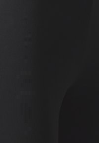 Leggings noirs, présentant une texture côtelée. Le tissu est lisse, avec un design ajusté qui épouse la forme des jambes.