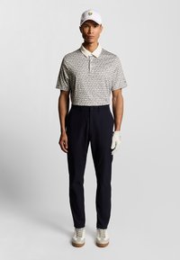 Kortärmad mönstrad polo skjorta i beige och svart, i kombination med mörkblå byxor. Tillbehör inkluderar en vit keps och en golfhandske.