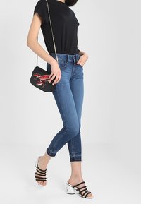 Svart t-shirt med kort ärm, blåa skinny jeans, svart handväska med röda accenter, och svarta strappy klacksandaler med en vit marmorblock-hæl.