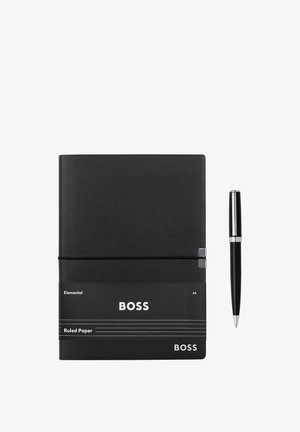 Juodas A5 formato linijuotas popieriaus užrašų knygutė su užrašu „BOSS“ ir šalia jos padėtas juodas rašiklis su sidabrinėmis detalėmis, ant balto fono.