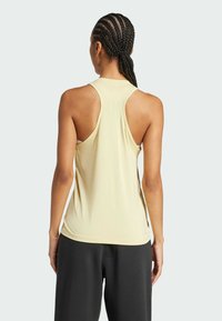 Top deportivo de color amarillo claro con escote redondeado y diseño de espalda nadadora. Textura suave y elástica con aberturas laterales; combinado con pantalones negros.
