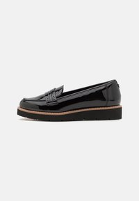 Mocassins en cuir verni noir avec un bout arrondi, des coutures décoratives et une semelle en caoutchouc, offrant une plateforme basse pour un confort supplémentaire.