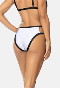 Białe majtki bikini z czarnymi wykończeniami, z teksturowanym wzorem i wycięciami na biodrach. Zaprojektowane w średnim stanie.