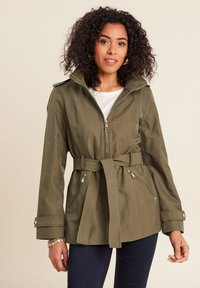 Olijfgroene, met een riem afgewerkte jas met capuchon. Bevat ritszakken, een ritssluiting aan de voorkant en knoopsluiting bij de mouwen. Gemaakt van een gladde, duurzame stof.