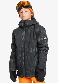 Svart mönstrad snowboardjacka med dragkedja fram, justerbar huva och svarta handskar. Bäraren har på sig orange skidglasögon och en mössa.