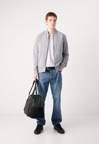 Jacheta bomber gri deschis cu un finisaj neted, asociată cu un tricou alb simplu și blugi albastri. Geantă din material negru cu două mâner.