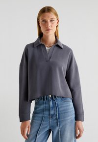Grå cropped sweatshirt med krave, med V-udskæring og lange ærmer. Bæres med højlaede blå denim jeans.