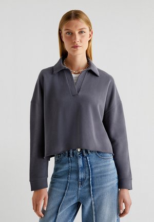 Grijze cropped sweatshirt met een kraag, voorzien van een V-halslijn en lange mouwen. Draagt met hoge taille blauwe denim jeans.