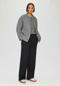 Grijze textuurjacket met een ronde kraag, gecombineerd met een grijze top, zwarte wijde broek en beige sneakers met witte accenten.