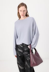 Hellviolettes, oversized Sweatshirt mit überschnittenen Schultern, kombiniert mit schwarzen Lederhosen. Hält eine tief burgunderrote Handtasche mit einem eleganten Design.