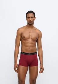 Bordeauxrode boxershorts met een zwarte tailleband waarop het "BOSS"-logo staat. De stof oogt glad en de pasvorm is aansluitend.