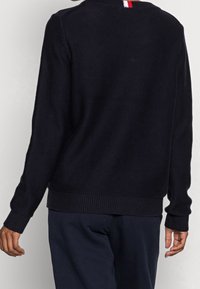 Granatowy sweter dziany z ribbowym wykończeniem dołu i rękawów oraz trójkolorowym akcentem na kołnierzu z tyłu. Miękka tekstura i klasyczny krój.