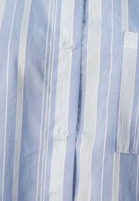 Camicia a righe blu chiaro e bianca, realizzata in cotone, con apertura frontale a bottoni trasparenti e taschino sul petto. Tessuto texturizzato.