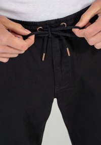 Pantalones de chándal negros con cintura elástica y cordón ajustable, con aglets de metal y una textura suave similar al denim.