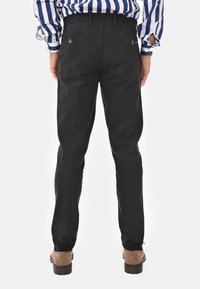 Pantaloni neri con vestibilità slim, dotati di due tasche posteriori, una texture liscia e polsini elasticizzati. Abbinati a scarpe marroni.