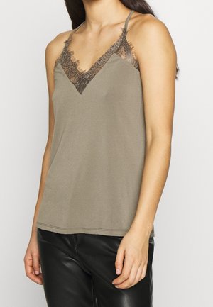 Olive green camisole with lace trim along a deep V-neck, thin adjustable straps, and a smooth texture. Styled with black fitted pants.