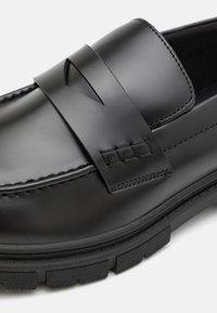 Schwarze Lederloafer mit genähtem Riemen und Ausschnittdetail. Verfügt über eine strukturierte Gummisohle mit einem gemusterten Profil für besseren Halt.