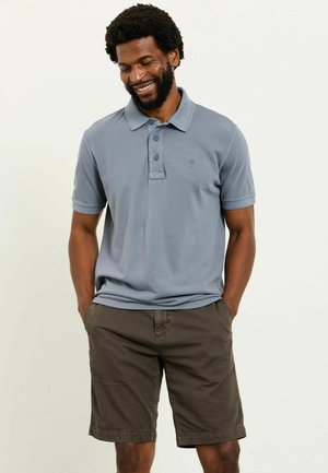 Graues Polohemd aus Baumwolle mit weicher Textur, Dreiknopfleiste und einem dezenten Logo, kombiniert mit olivgrünen Shorts.