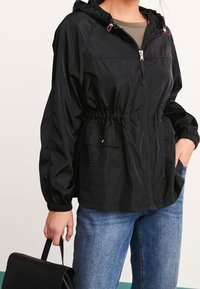 Czarna kurtka z kapturem, z elastycznym pasem, z zamkiem z przodu, bocznymi kieszeniami i różowymi akcentami. Nosi się ją na zieloną bluzkę i zestawia z niebieskimi dżinsami.