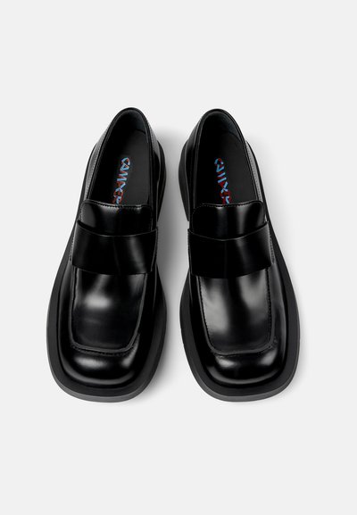Mocassins en cuir noir avec une large sangle sur le dessus, bout carré, semelle épaisse et design minimaliste. Texture douce et polie.