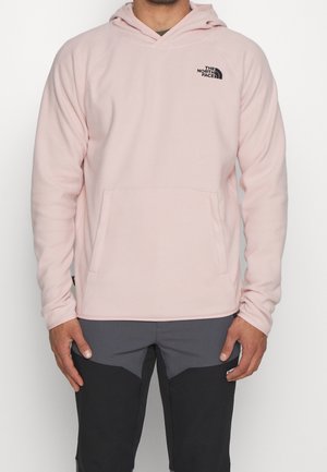 Sudadera con capucha de color rosa claro hecha de forro polar suave; cuenta con un bolsillo tipo canguro y un logo negro en el pecho. Textura suave y ajuste relajado.