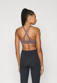 Καφέ αθλητικό μπουστάκι με σχεδιασμό racerback, λεπτομέρεια κοψίματος και υφασμάτινη υφή, σε συνδυασμό με ψηλόμεσα μαύρα κολάν.