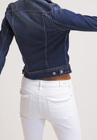 Denimjacka i mörkblått med figurnära design, fickdetaljer och knappritningar. Matchad med vita jeans med bakfickor.