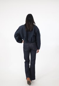 Granatowa krótka bluza z obszernymi rękawami i elastycznym dołem, zestawiona z ciemnymi dzwonowymi dżinsami i brązowymi butami na obcasie, widziana od tyłu.