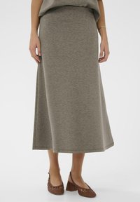 Pelēka, potītes garuma svārki, izgatavoti no mīkstas auduma ar gludu tekstūru, ar brīvu siluetu un vienkāršu dizainu. Pāris ar brūnām austām kurpēm.